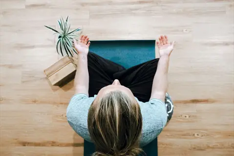 overhead view of a person practicing body scan meditation on a yoga mat, hands in meditative gesture with potted plant and wooden blocks nearby