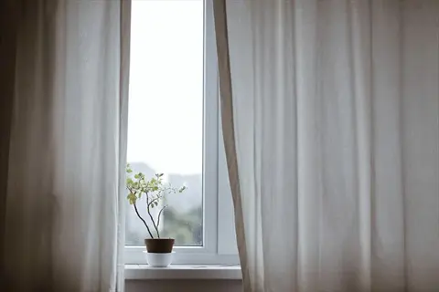 partially open light-filtering blackout curtains in a bedroom window with potted plant on sill - light management