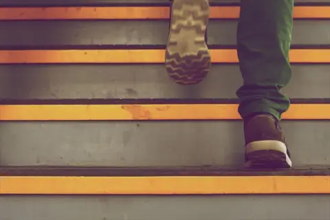 person climbing stairs in a building, low section view showing shoes on yellow-edged steps