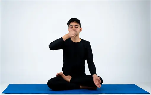 person in black meditation attire demonstrating alternate nostril breathing hands technique on blue yoga mat (right hand positioned near face)