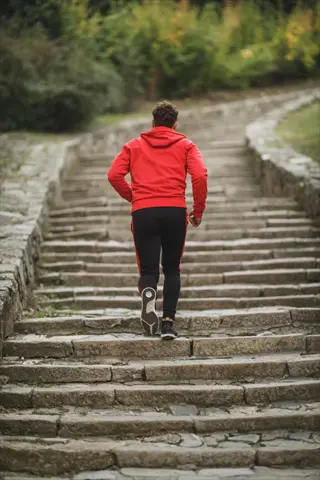 person in red hoodie climbing stone stairs in a green outdoor park setting
