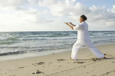person in white performing qigong morning practice on serene beach, embodying eight brocades movement against ocean backdrop