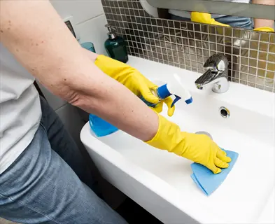 person in yellow gloves cleaning a bathroom sink with a blue cloth and spray bottle (cloth is being used as homemade cleaning wipes for disinfection)