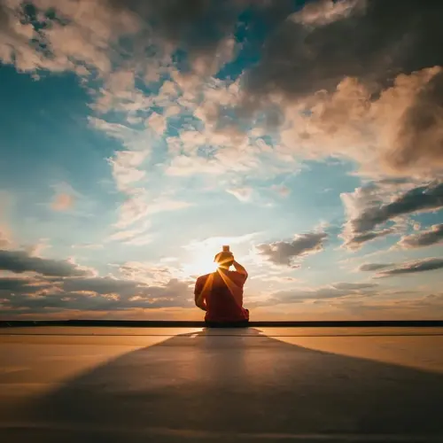 person meditating at sunrise, silhouette against vibrant sky with clouds