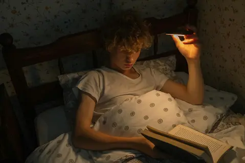 person reading before bed under dim light with open book, demonstrating a pre-sleep routine