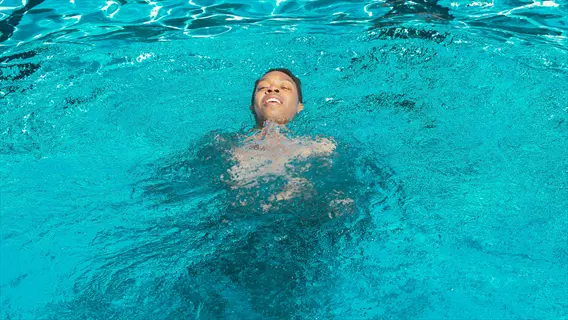 person swimming in bright blue pool water with face visible above surface