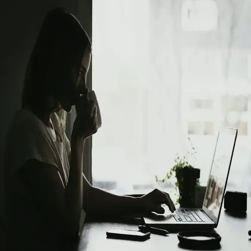 person using computer eye comfort in naturally lit room, sipping from cup