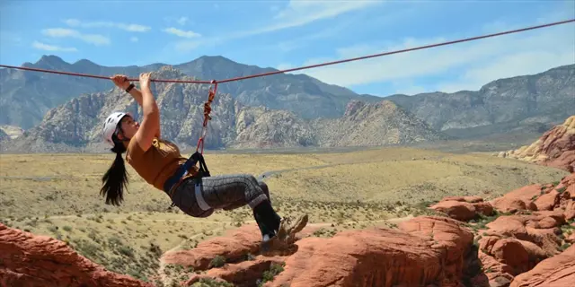 person ziplining during a rock climbing adventure in a desert canyon with mountain views, embodying adventure therapy