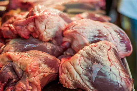 pile of raw beef hearts with visible textures and fat, displayed at a market or butcher shop