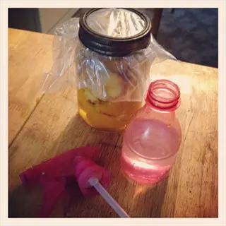 pink vinegar cleaning spray bottle next to a jar with plastic wrap on a wooden table, diy cleaning context