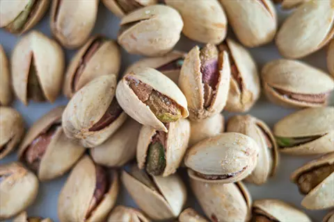 pistachio nuts in shells (some open, some closed) with visible green kernels and salt crystals on a light background