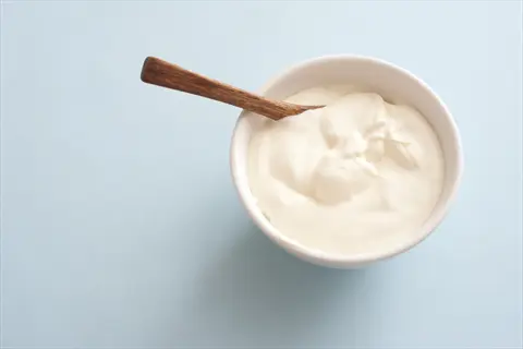 plain greek yogurt in a white bowl with a wooden spoon on a light blue background