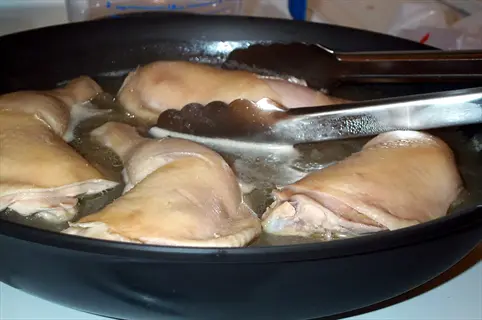 poached chicken breast pieces cooking in a pan with tongs and broth