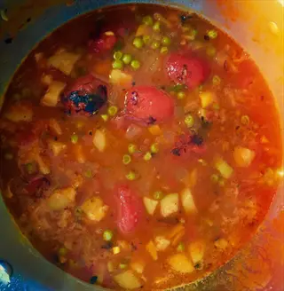 pot of roasted vegetables broth with charred tomatoes, peas, and mixed vegetables