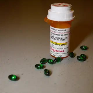 prescription bottle of ergocalciferol capsules (vitamin d2 50,000 iu) on countertop with scattered green capsules. label shows patient name, dosage instructions (1 capsule bi-weekly), and pharmacy details
