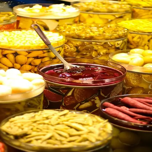 probiotic foods assortment in glass jars: pickled vegetables including beets, beans, carrots, and more; slotted spoon in one