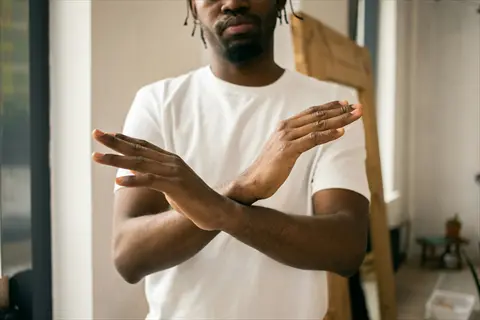 professional saying no with crossed arms gesture in white t-shirt against office backdrop