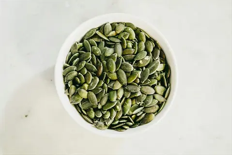 raw pumpkin seeds in a white bowl on a light marble surface - nutrient-rich snack