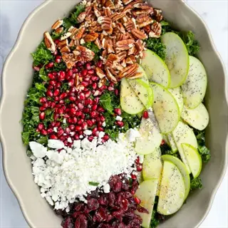 raw vegetable salad featuring kale, pomegranate seeds, feta cheese, dried cranberries, green apple slices, and pecans