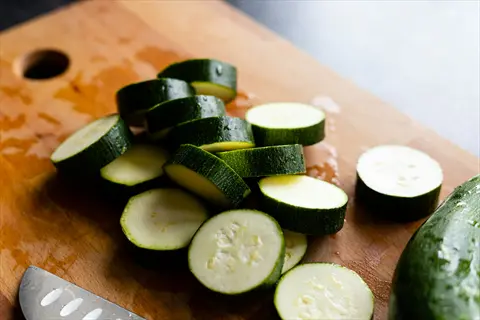 raw zucchini slices on a wooden cutting board with a kitchen knife