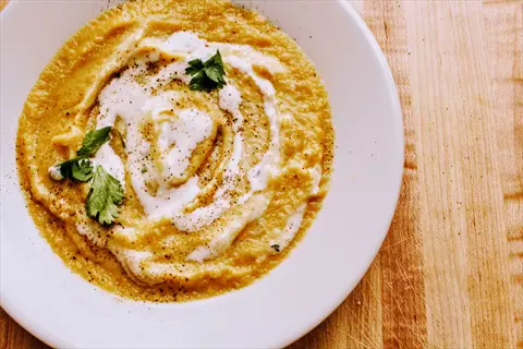 red lentil dip close-up in white bowl with creamy swirl, cilantro garnish, and spice sprinkle on wooden surface