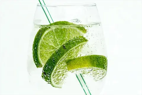 refreshing glass of sparkling water with lime slices, bubbles, and green straw against white background