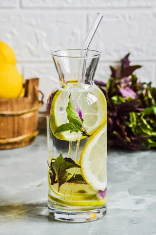 refreshing water hydration with lemon slices and herbs in a glass carafe, surrounded by whole lemons
