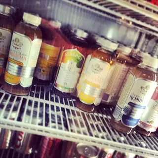 refrigerator shelf displaying various kombucha bottles with visible labels, arranged among other beverages