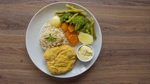 restaurant meal healthy: golden fried protein, brown rice, steamed broccoli, green beans, carrot slices, boiled egg, and creamy dipping sauce on wooden table