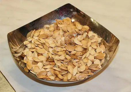 roasted pumpkin seeds in a metallic bowl on a marble countertop - close-up of light brown toasted seeds with visible seasoning