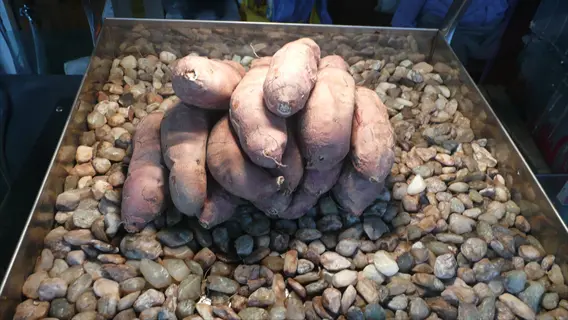 roasted sweet potatoes displayed on stones in a metal tray at a market