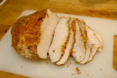 roasted turkey breast with seasoned crust, partially sliced on white cutting board with crumbs on wooden countertop