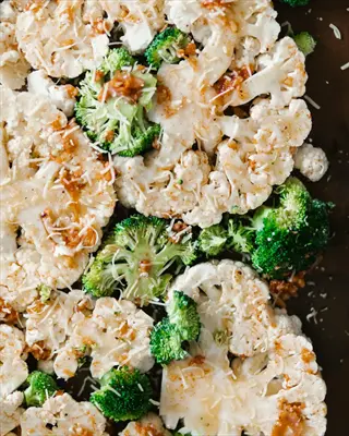 roasting vegetables sheet pan prep featuring cauliflower steaks and broccoli florets with grated cheese seasoning