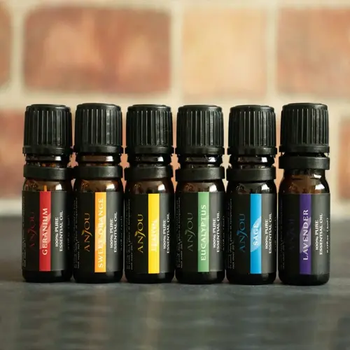 row of anjou essential oil bottles including geranium essential oil bottle, sweet orange, lemon, eucalyptus, sage, and lavender on dark surface against brick wall