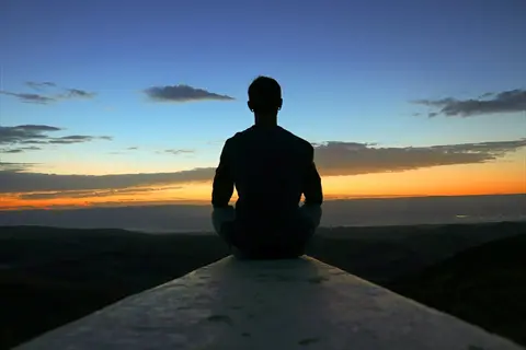 silhouette of a calm person in nature meditating at sunset over mountains, embodying emotional resilience