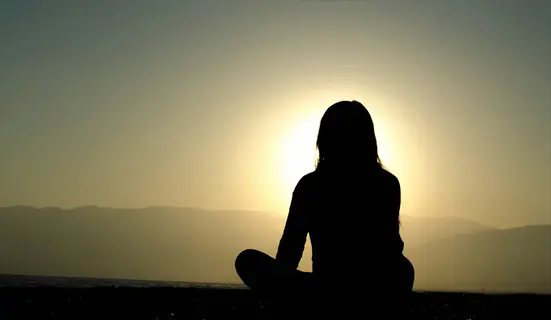 silhouette of person meditating at sunrise over mountains and calm water, embodying anxiety relief morning through preventative morning routine