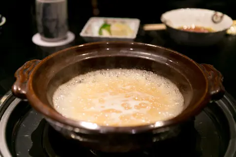simmering broth cooked rice in a traditional clay pot on a stove, with other dishware in background