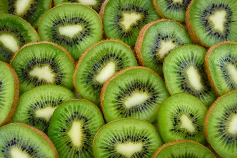 sliced kiwi fruit cross-sections with vibrant green flesh, black seeds, and brown fuzzy skin arranged in a patterned background
