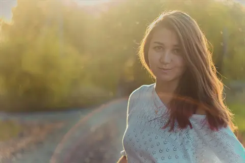 smiling morning person outdoors: woman with warm golden sunlight on face, surrounded by trees in serene natural setting