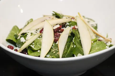 spinach salad with sliced pears, dried cranberries, and cheese in a white bowl, paired with olive oil for a healthy diet