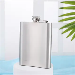 stainless steel jacket pocket bottle (hip flask) on pedestal stand against bright background with tropical leaf