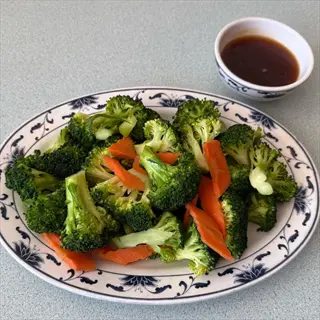 steamed broccoli plate with carrots and dipping sauce on a blue floral patterned dish
