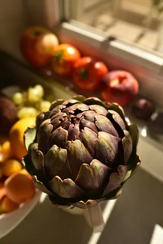 steamed whole artichoke as centerpiece with surrounding fresh fruits in sunny kitchen setting