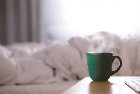 steaming green coffee mug on bedside table in sunlit bedroom, symbolizing alert morning coffee for daytime alertness boost