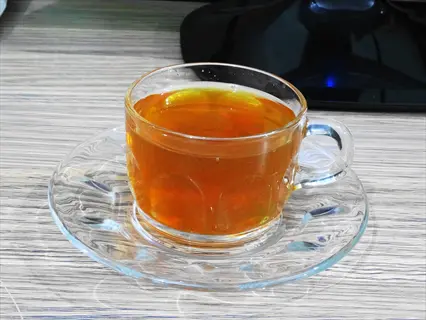 steaming lemongrass tea in clear glass cup with matching saucer on wooden surface