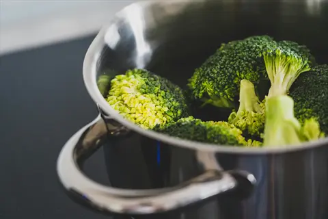 steaming vegetables: fresh broccoli florets in a stainless steel pot on a stovetop. illustrates a cooking preservation method for nutrient retention