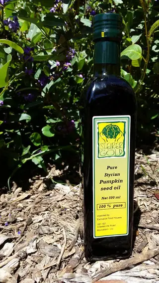 steirer gold pumpkin seed oil bottle (styrian, 500ml) on natural mulch with green foliage and purple flowers in the background