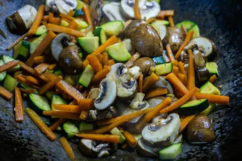 stir fry vegetables with mushrooms, carrots, and zucchini in a wok