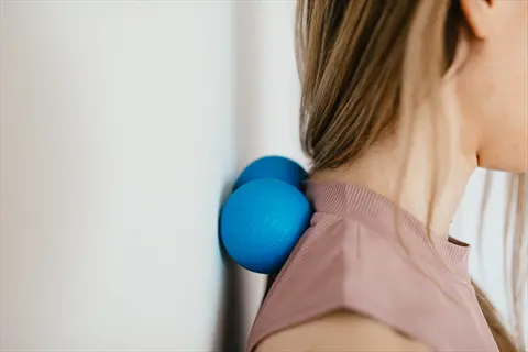 tennis ball back massage: woman using blue massage balls against a wall for self upper back and neck relief