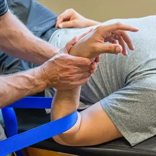 therapist performing forearm massage using blue strap on male client's arm during physical therapy session, demonstrating forearm and elbow ease techniques